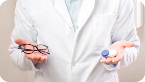 Врач держит на ладони правой руки очки, на ладони левой руки линзы